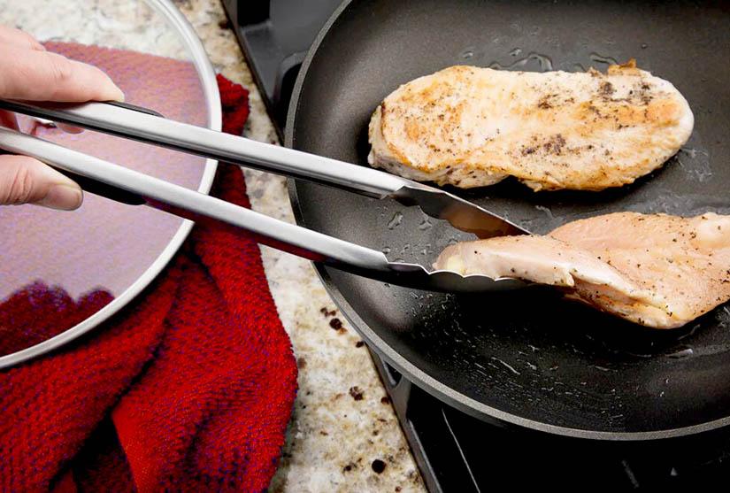 A man grabbing a steak with a pair of tongs