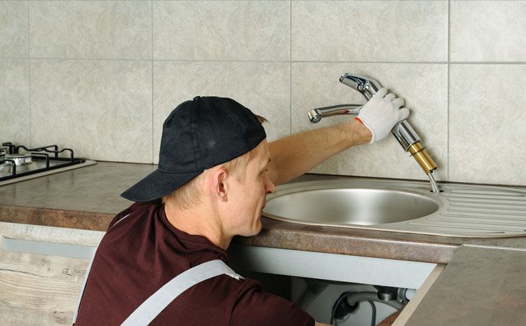 A plumber fixing a sink, illustrating part of the process of how to replace kitchen faucet